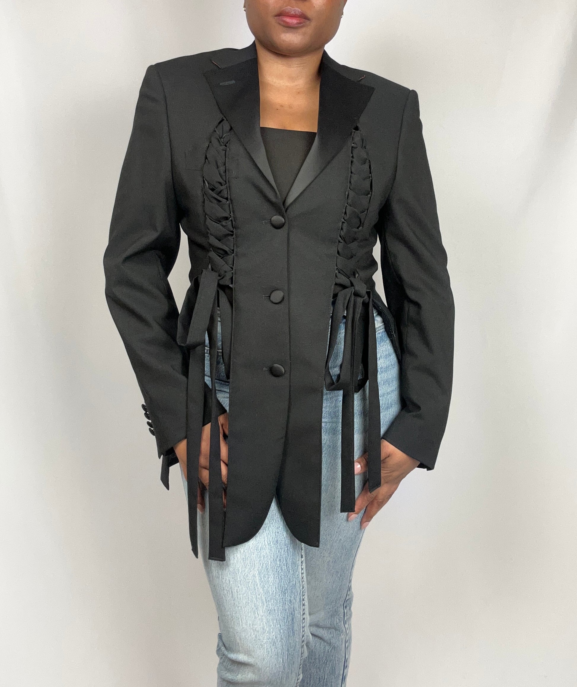 Black blazer with plaited strap details worn by a person on a plain background