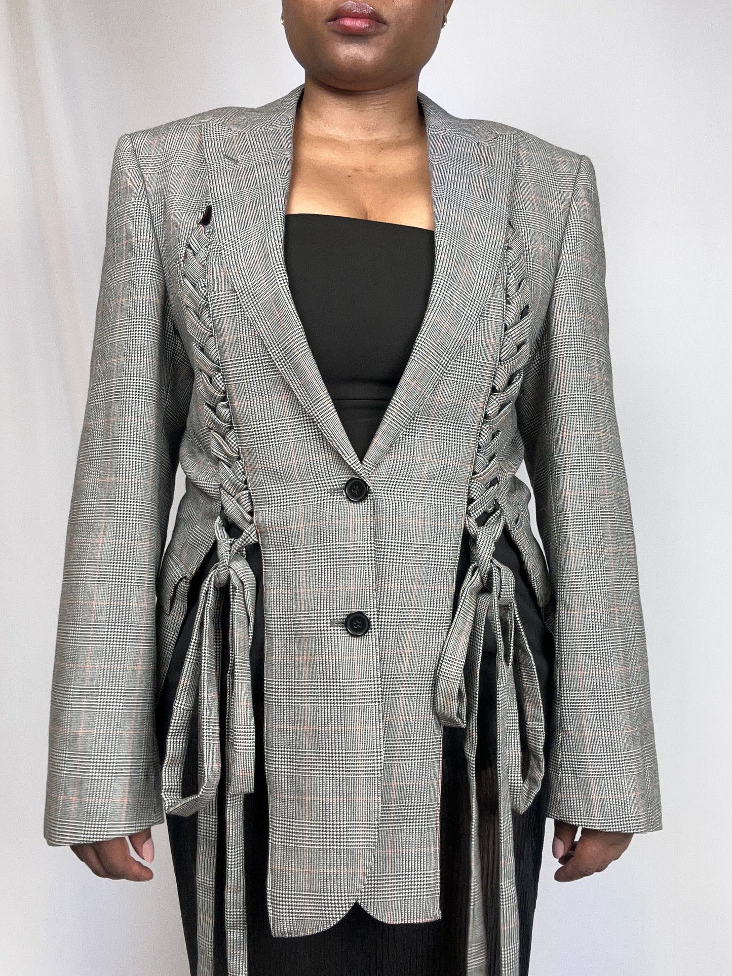 Person wearing a checkered blazer with braided details on a white background