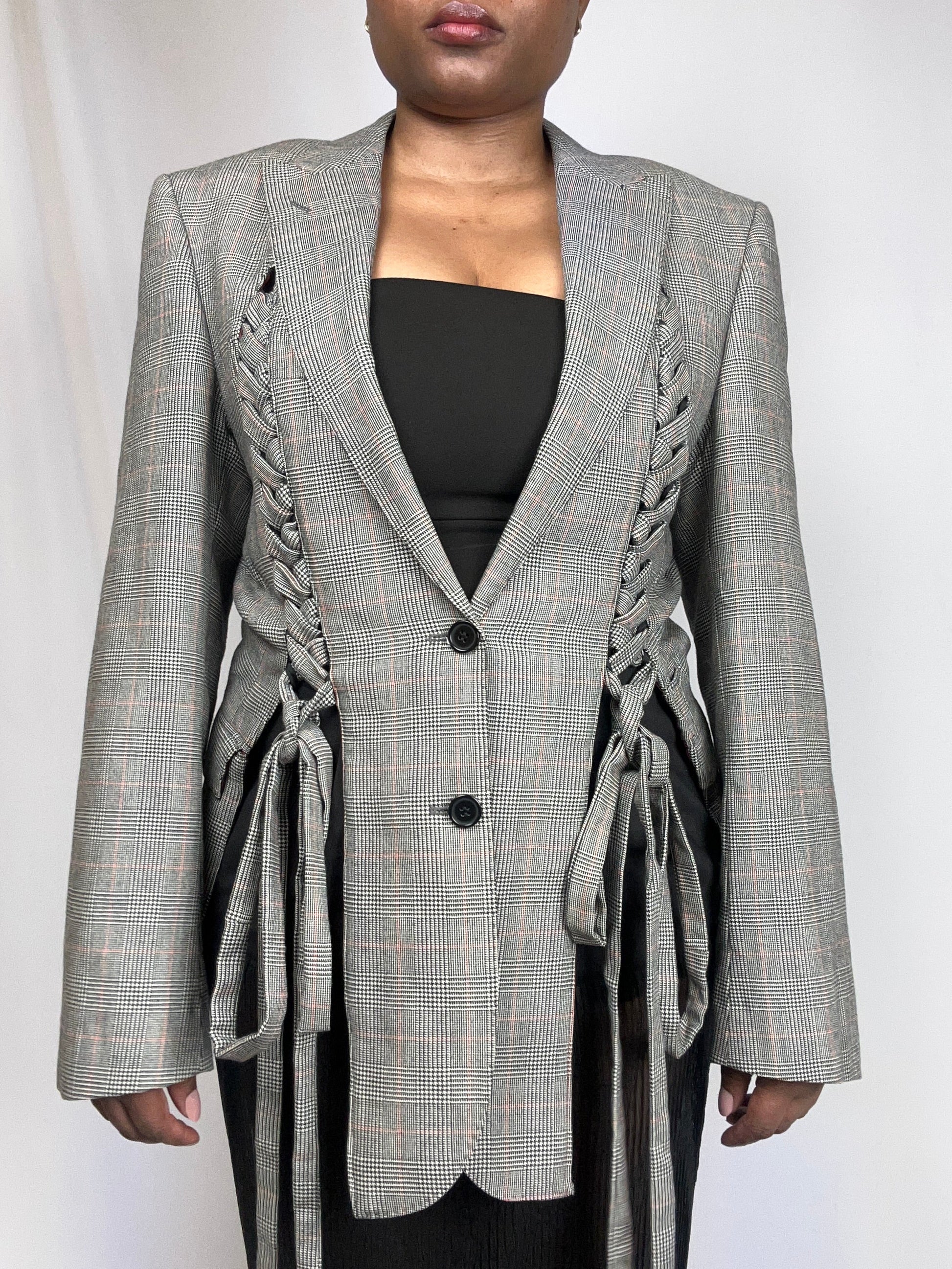 Person wearing a checkered blazer with braided details on a white background
